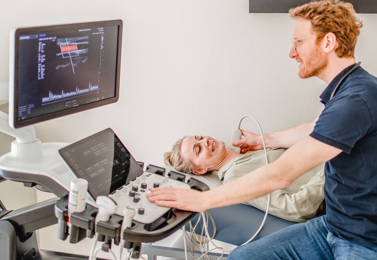 Arzt untersucht Gefäße mit Ultraschallgerät, Patientin liegt auf der Liege