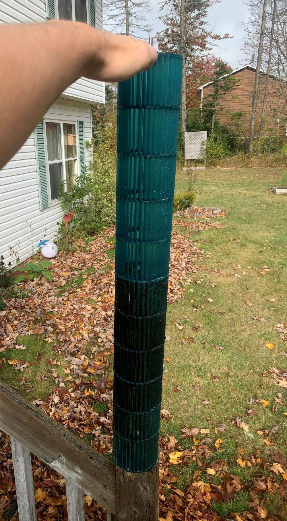 A person is holding a green fence post in front of a house.
