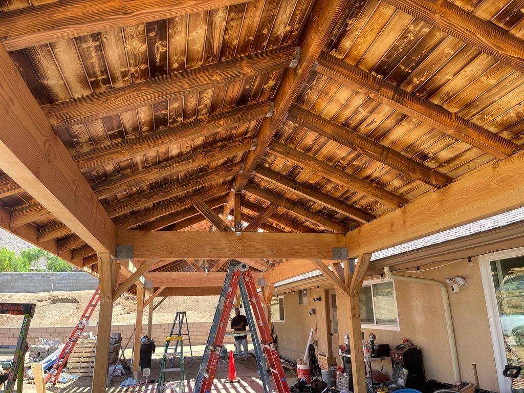 Wooden patio roof under construction; workers on ladders.