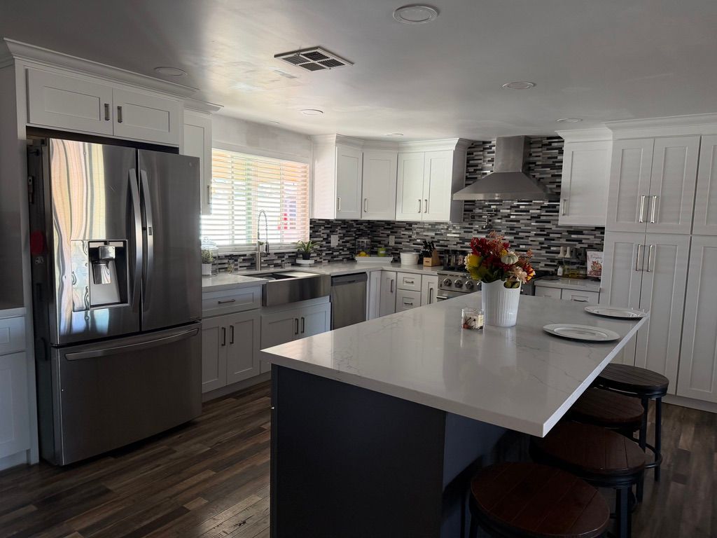 Modern white kitchen with stainless steel appliances, dark island, and a mosaic backsplash.
