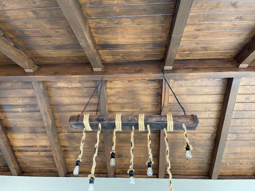 Wooden beam light fixture hanging from a wood plank ceiling.