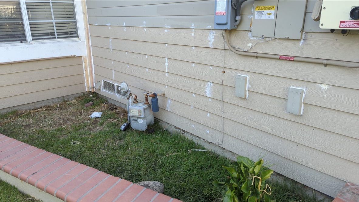 A gas meter and electrical panel on a beige-sided house next to a small lawn.