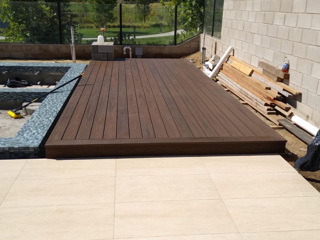 Wooden deck extending from a pool with blue tile edging, next to light-colored stone patio.