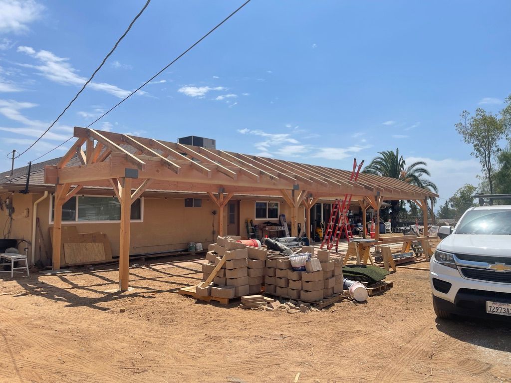 Construction of wooden patio cover attached to a tan-colored building; building materials and a white truck present.