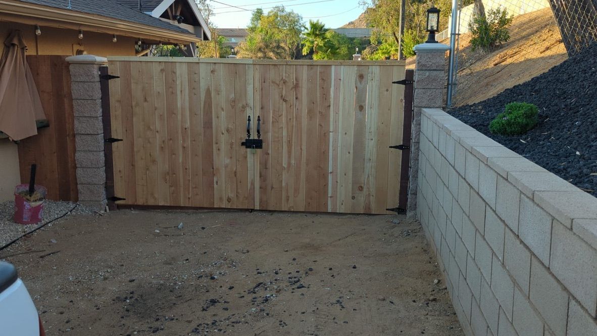Wooden gate with black hardware between brick columns, driveway.