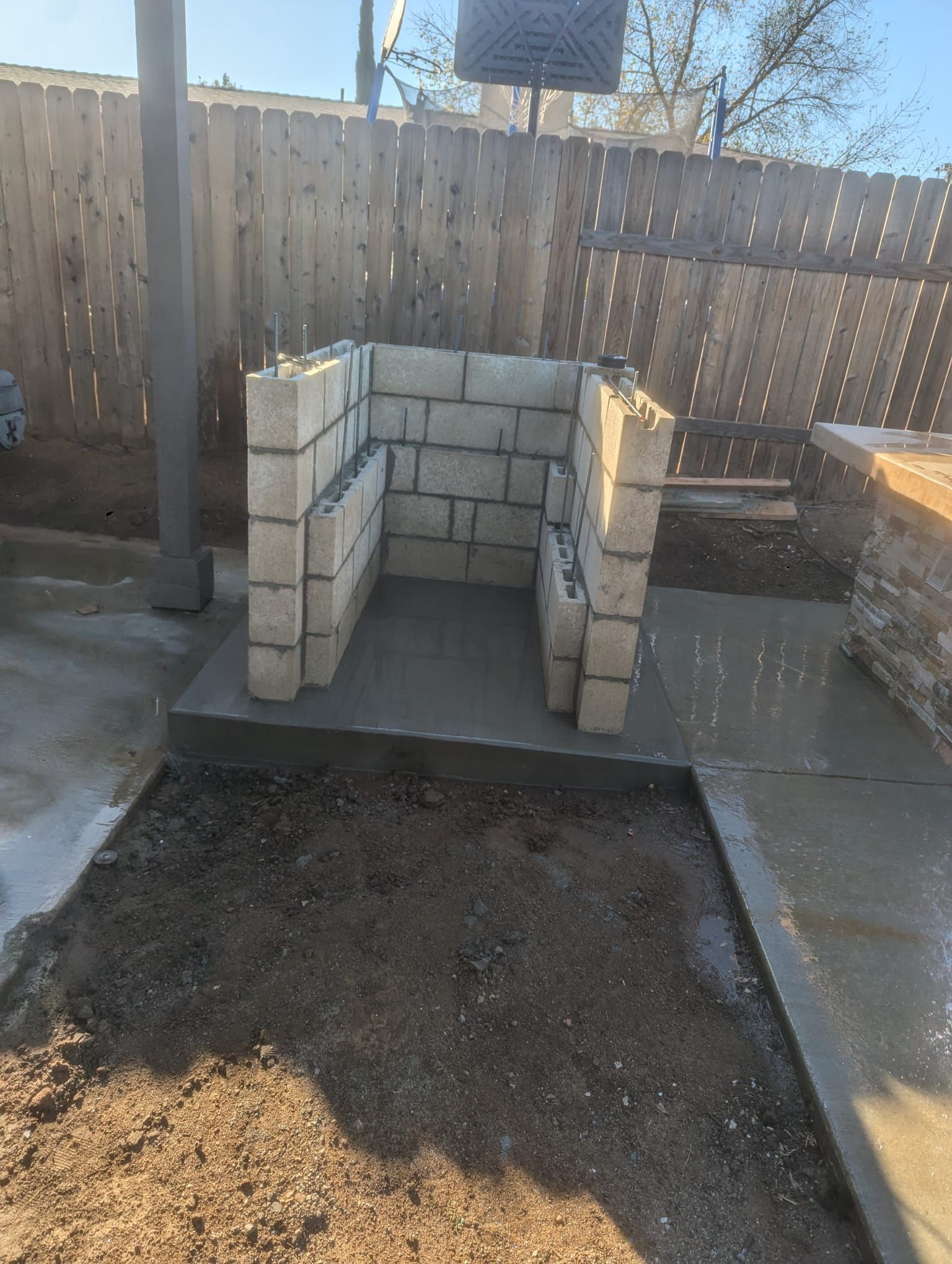 Concrete block structure under construction, on concrete slab in a yard.