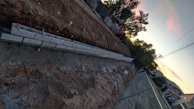 Retaining wall under construction on a hillside, using gray concrete blocks.