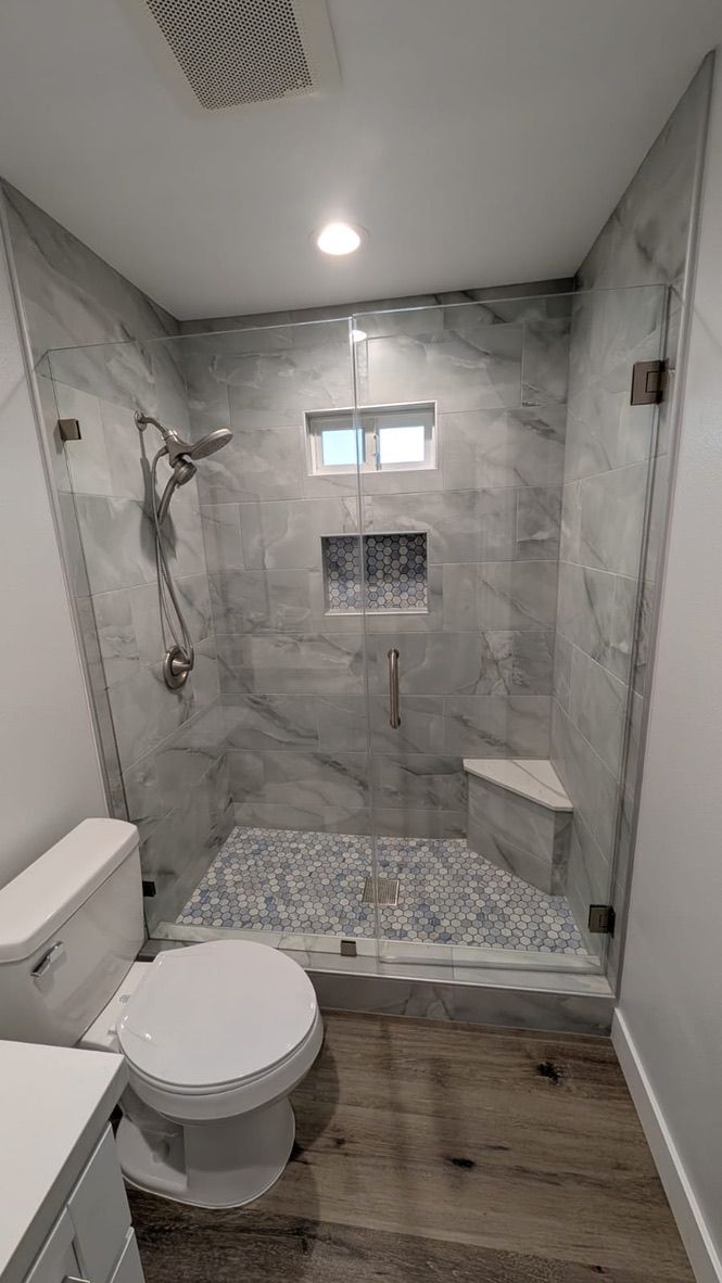 Modern bathroom with glass shower, marble tile, pebble floor, built-in bench, and wood-look tile.