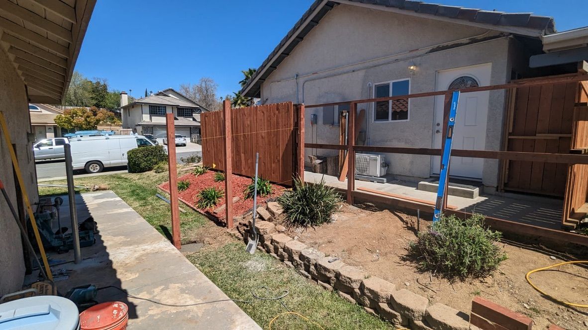 Backyard with new brown fence, landscaping, and house in the background on a sunny day.