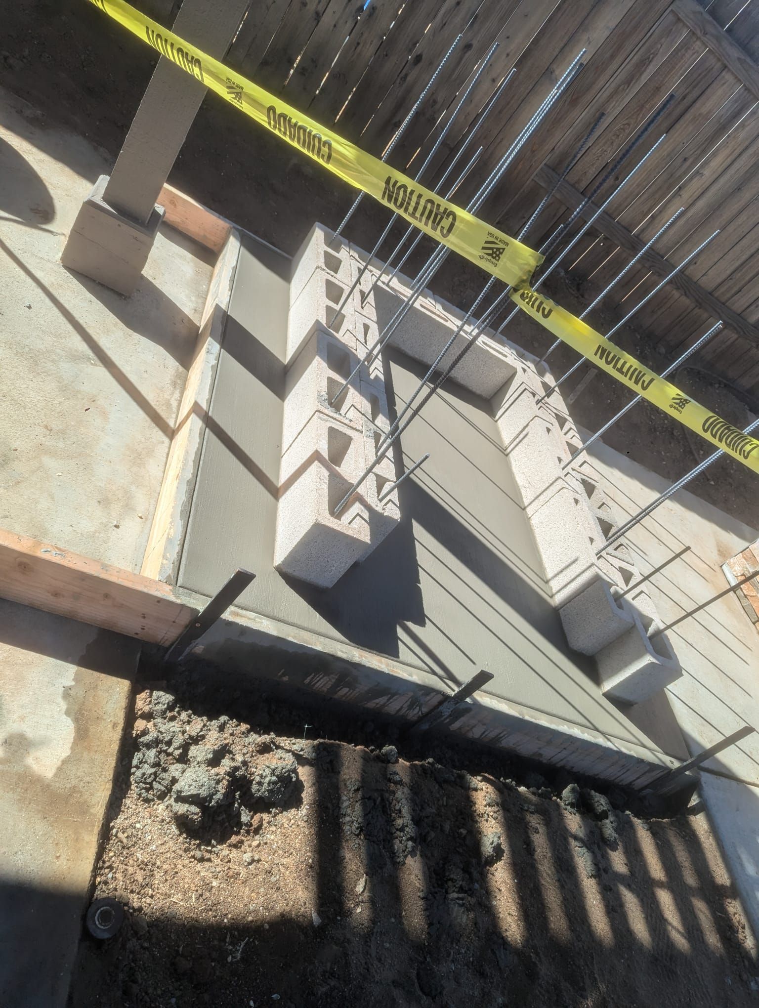 Construction site with gray concrete and cinder blocks, metal rebar, caution tape, and wooden frame.