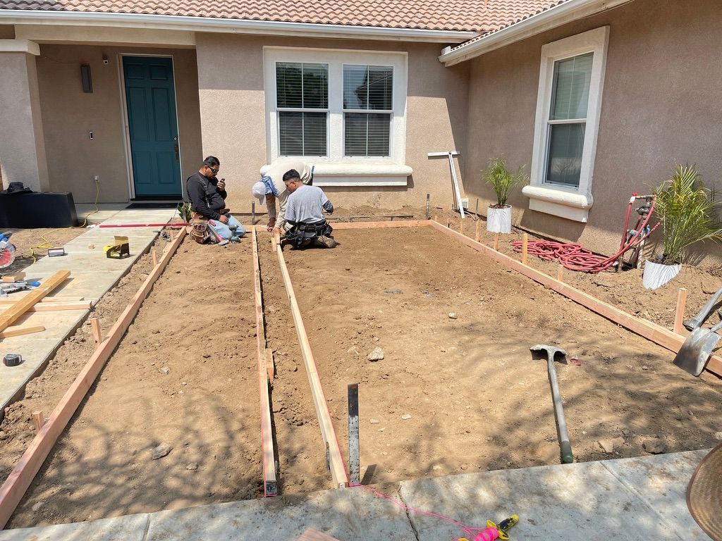 Construction workers building a concrete patio in front of a house. Wooden forms define the patio space.