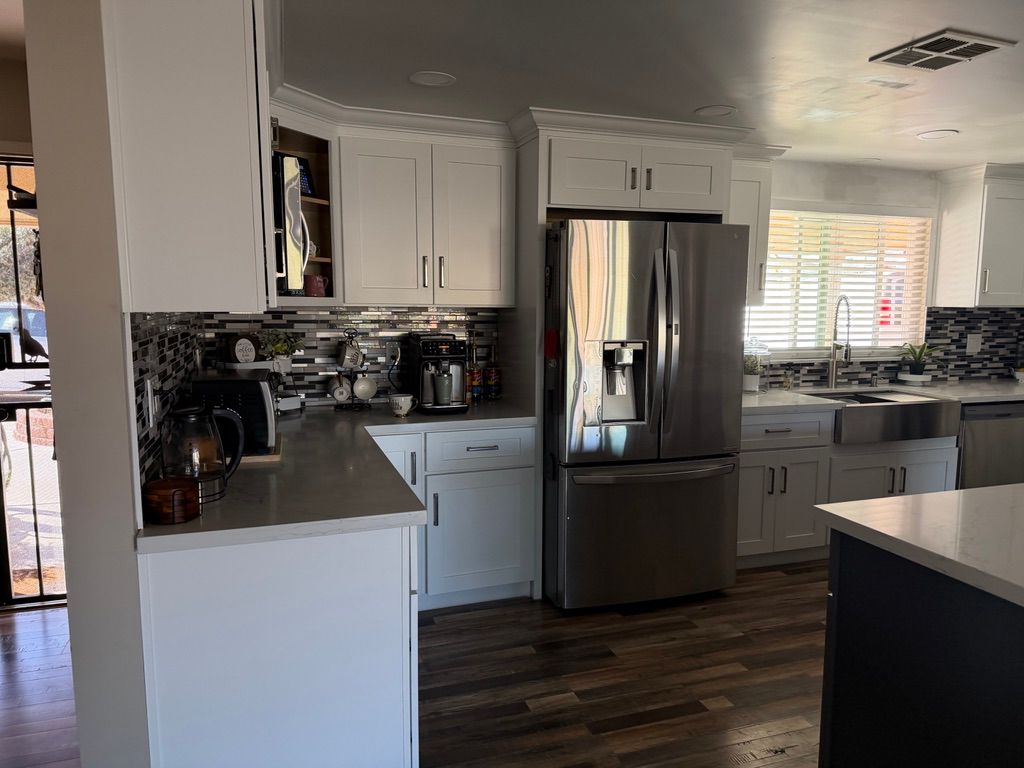 White kitchen with stainless steel appliances, cabinets, and countertops, and wood flooring.