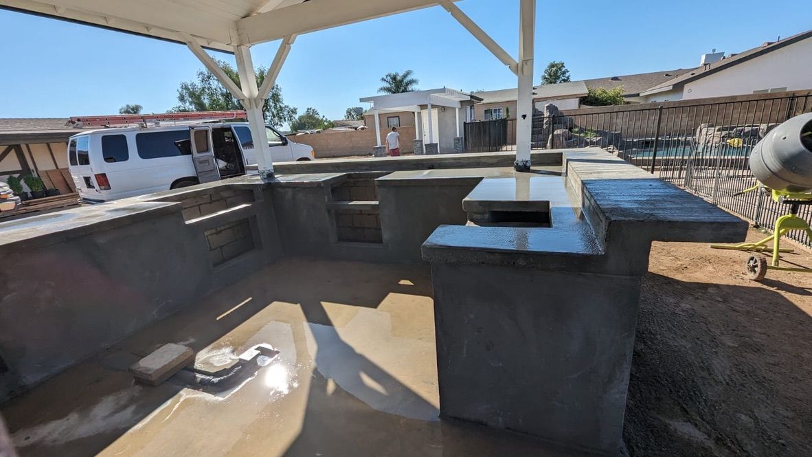 Outdoor concrete kitchen under construction, with a white canopy and a white van in the background.