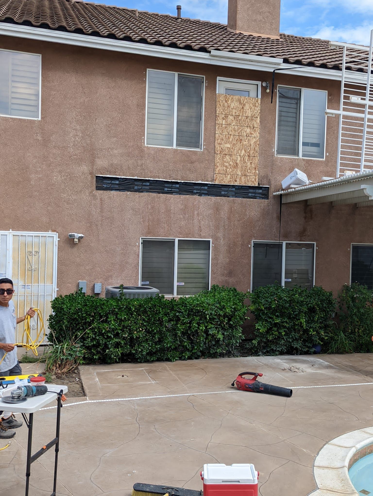 Backyard exterior with a house under repair, a ladder, and a person working.