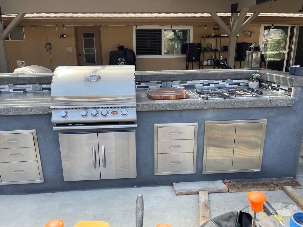 Stainless steel outdoor kitchen with grill, cooktop, and storage cabinets.