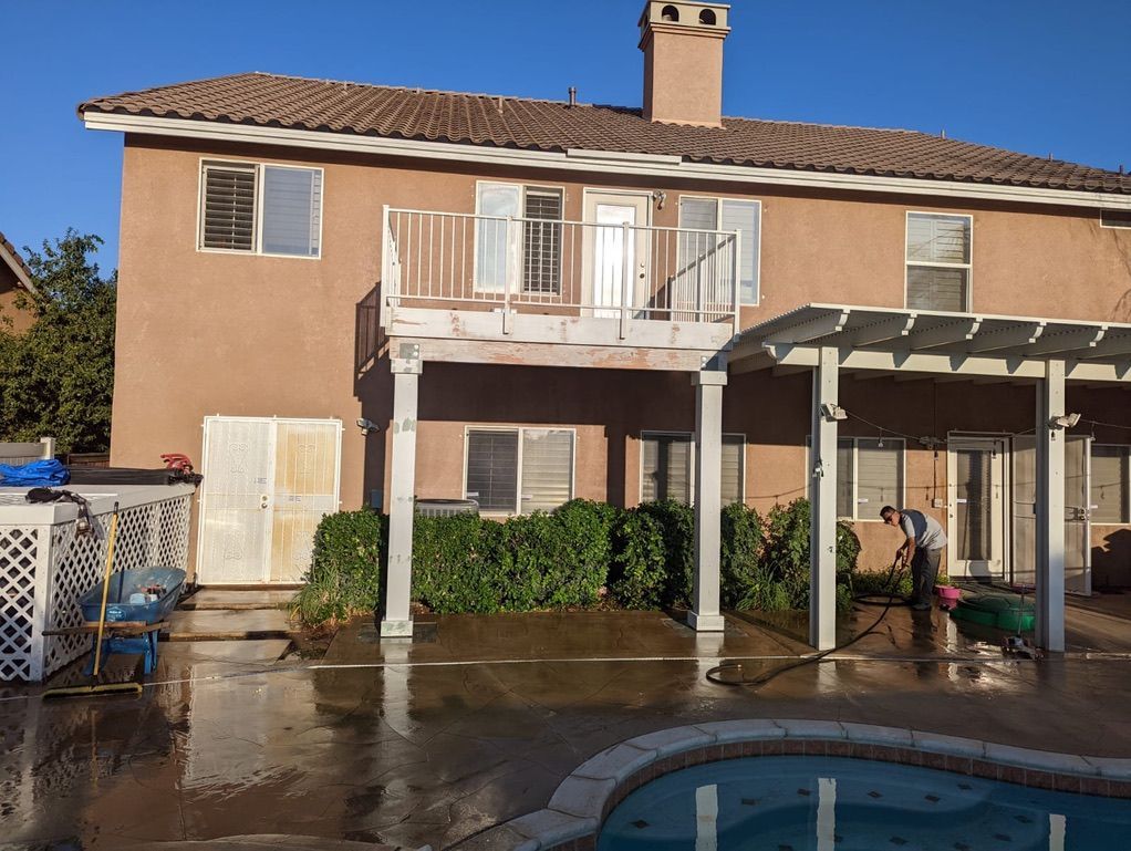 Backyard view: Two-story stucco house with balcony, pergola, pool, and a person watering plants.