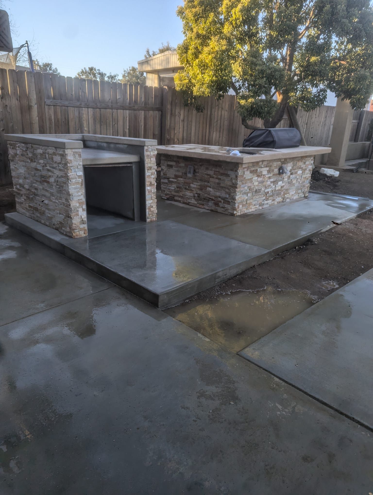 Outdoor kitchen with concrete countertops and stone facade. Includes a grill, built-in storage, and wet concrete patio.
