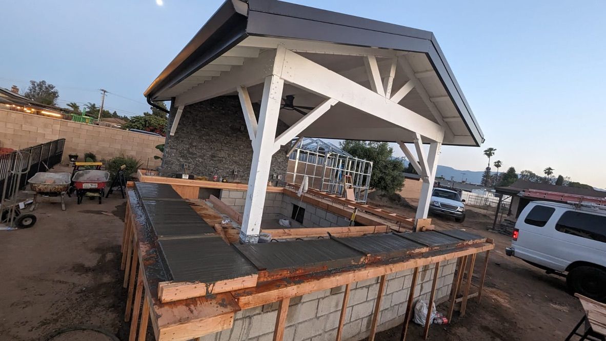 Outdoor bar under construction; white wood frame, gray roof, cinder block base, dirt setting.