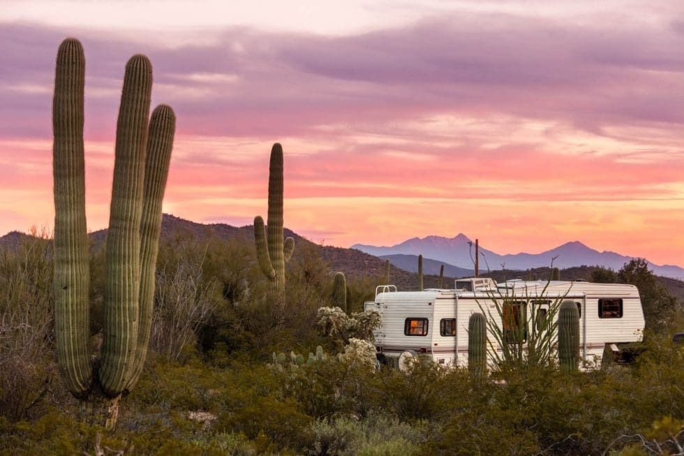 A rv is parked in the desert with cactus and mountains in the background.