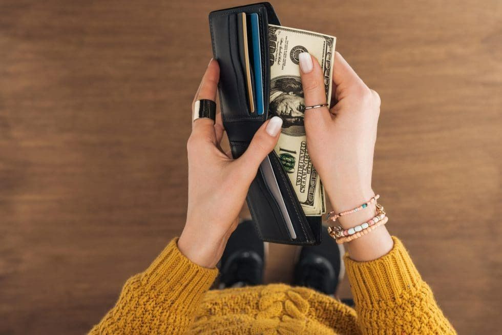 A woman is holding a wallet full of money and credit cards.