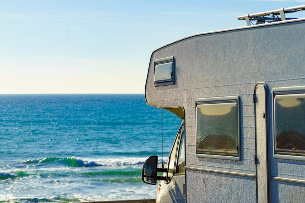 A rv is parked on the beach next to the ocean.