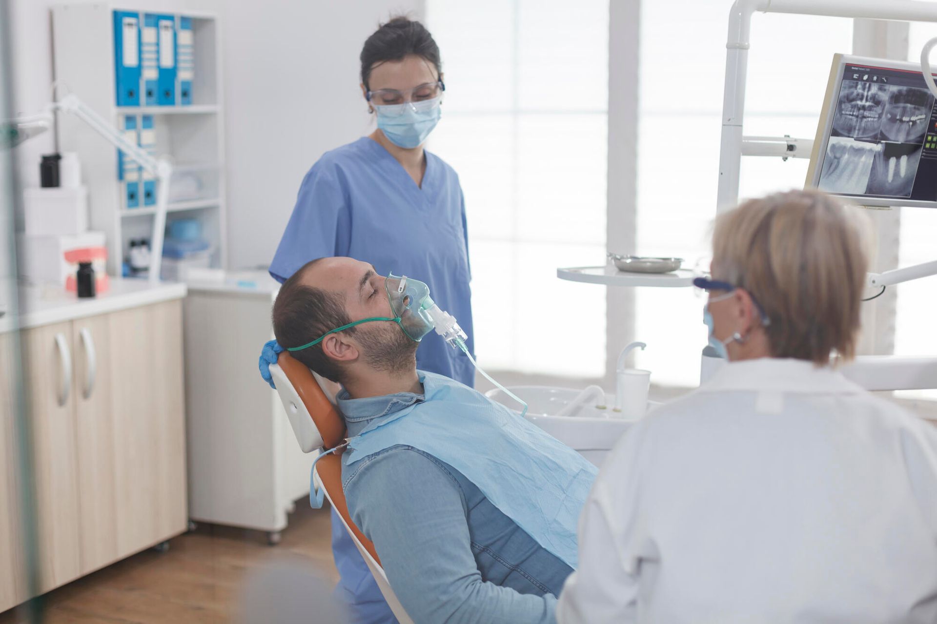 A man is sitting in a dental chair with an oxygen mask on his face.