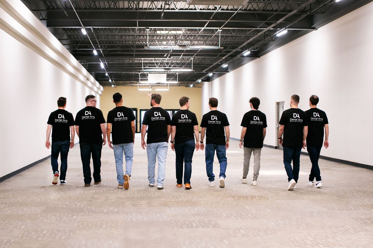 A group of men in black shirts are walking down a hallway.