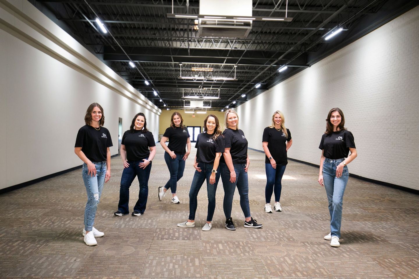 A group of women are posing for a picture in an empty hallway.