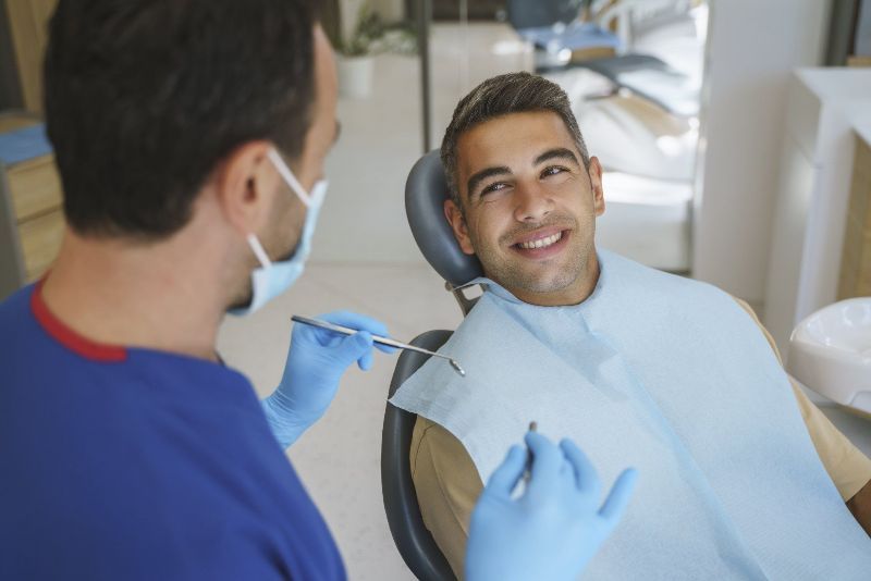 A man is sitting in a dental chair while a dentist examines his teeth.