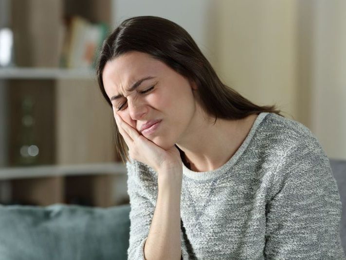 A woman is sitting on a couch with a toothache.