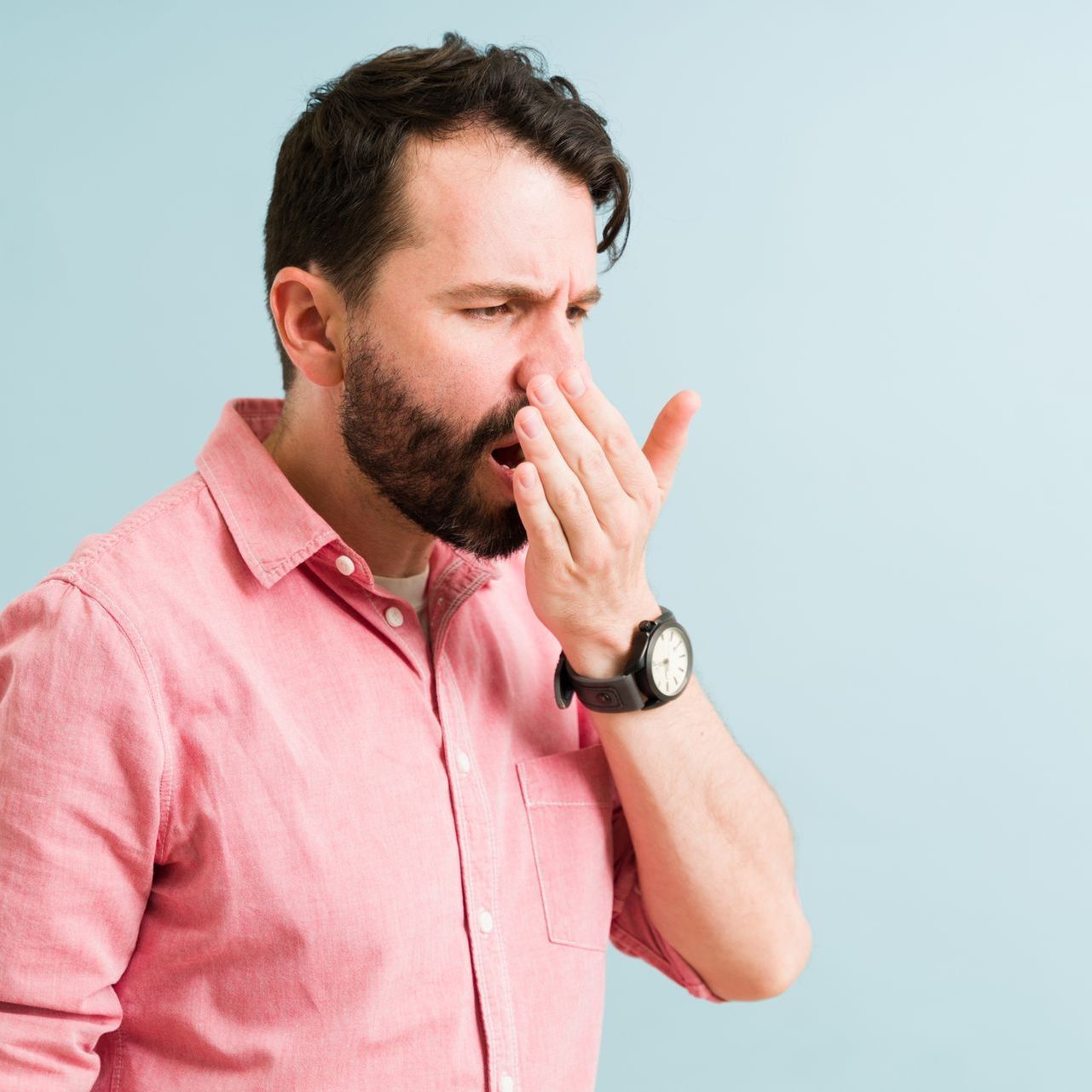A man in a pink shirt is covering his nose with his hand.