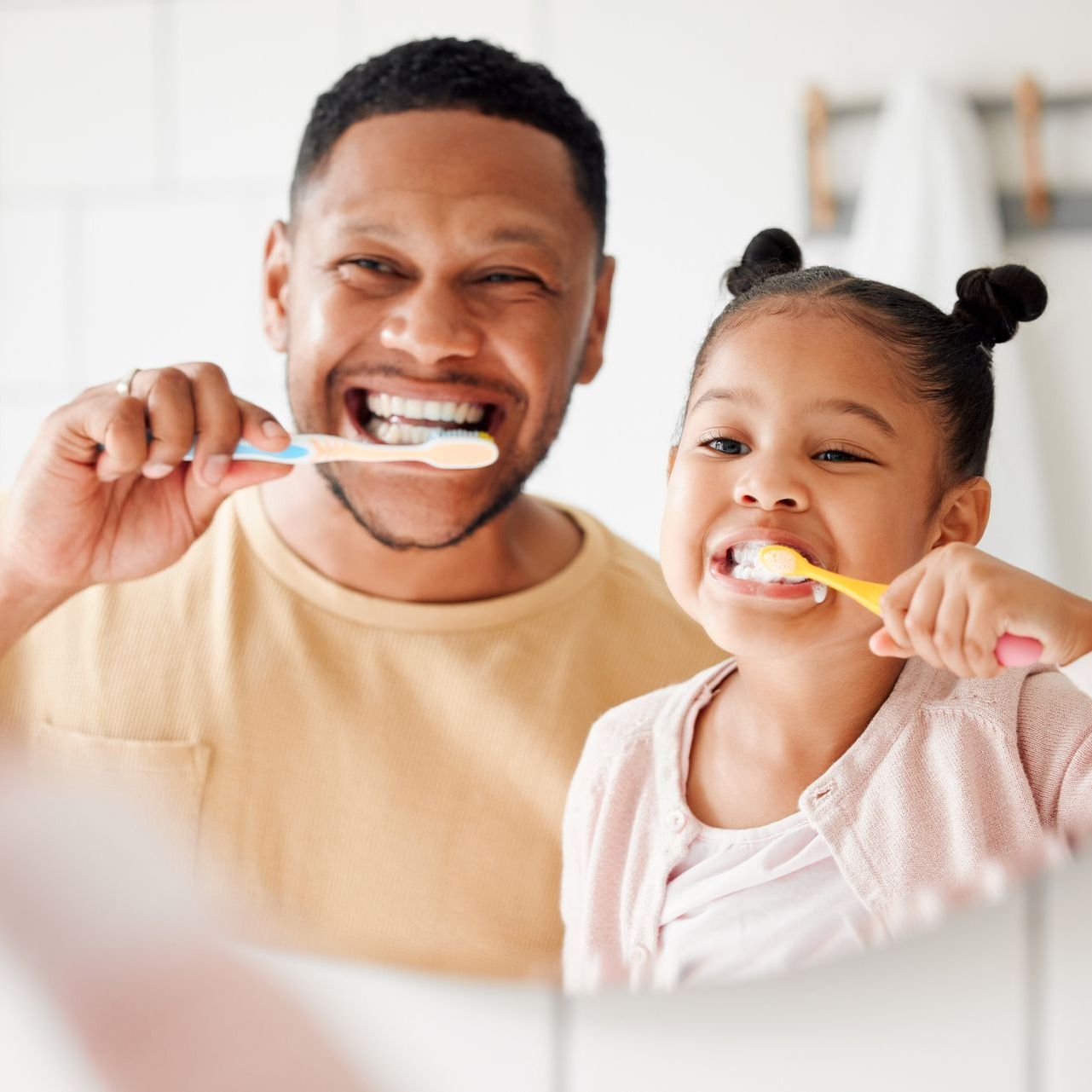 A man and a little girl are brushing their teeth in front of a mirror.