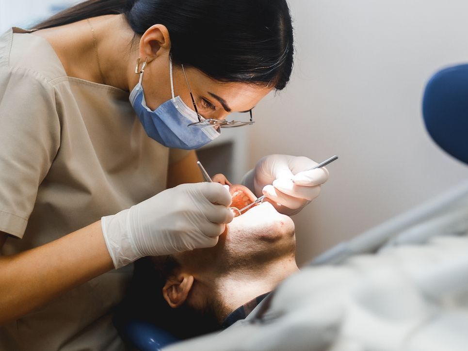 A female dentist is examining a man 's teeth in a dental office.