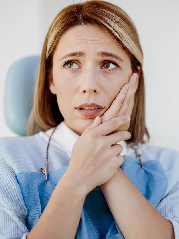 A woman is sitting in a dental chair holding her mouth in pain.