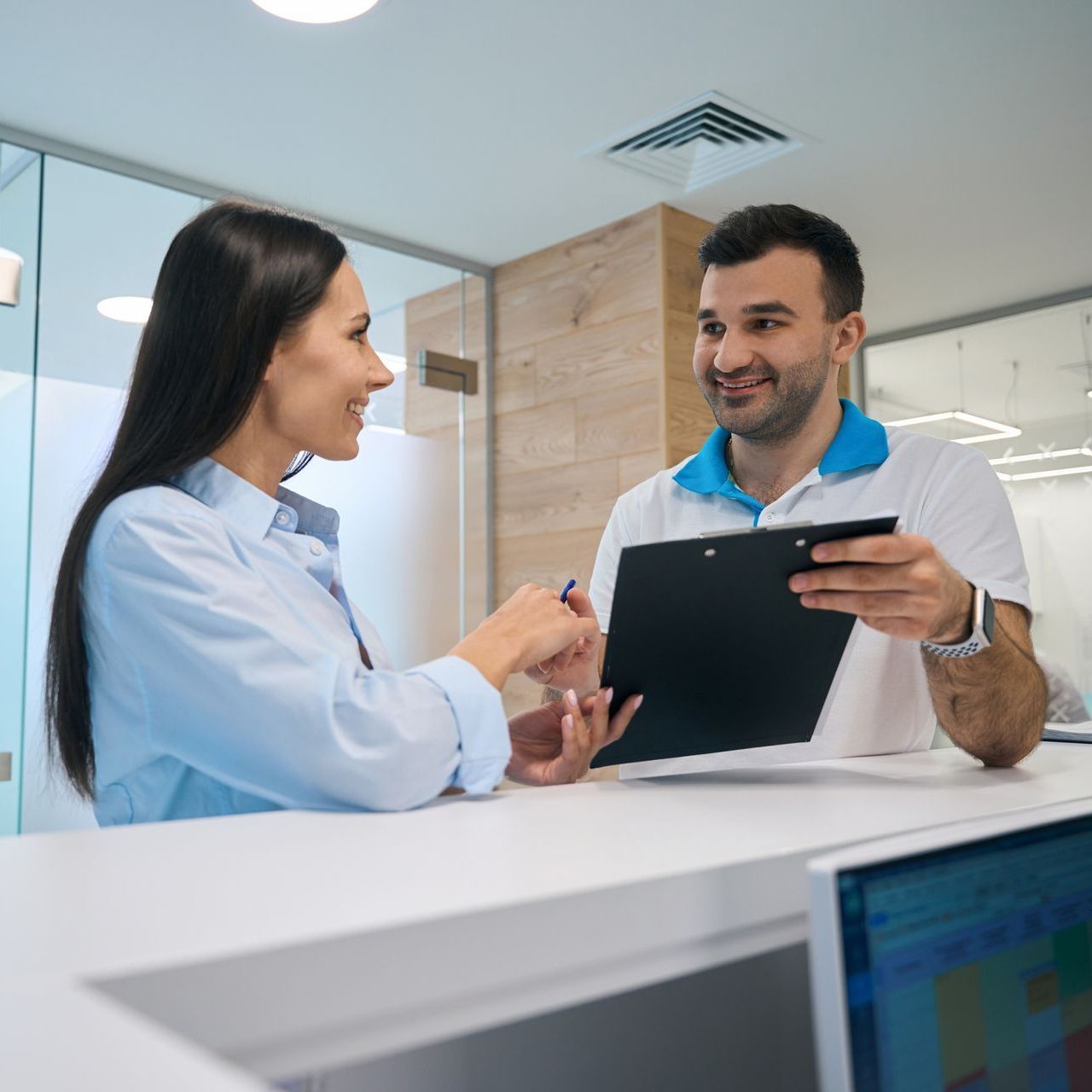 A man and a woman are sitting at a desk looking at a clipboard.