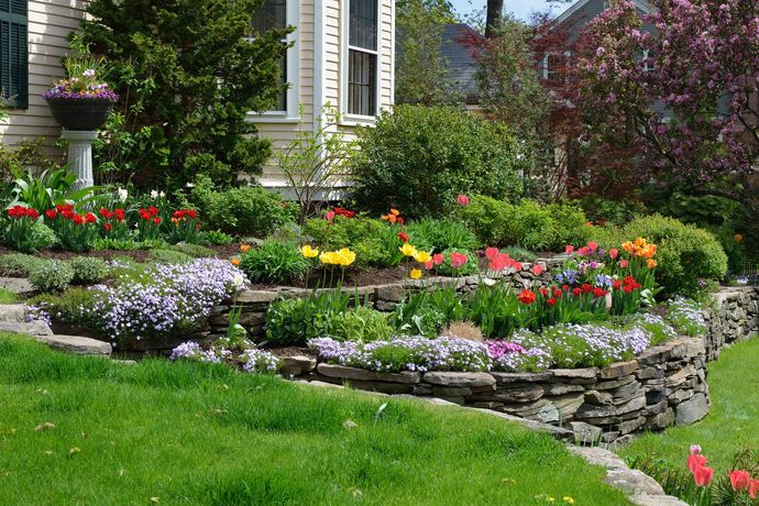Colorful flower garden with stone retaining wall and lush green lawn beside a house