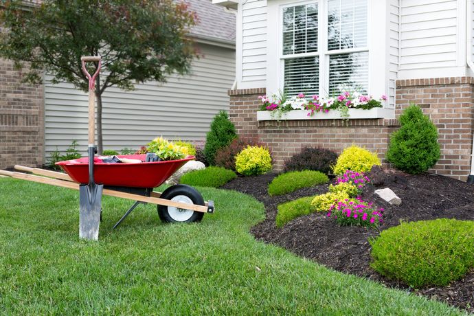 Red wheelbarrow beside a landscaped house garden with flowers and trimmed shrubs