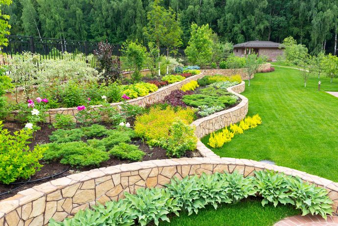 Curved stone garden beds with colorful flowers and greenery on a lush hillside landscape