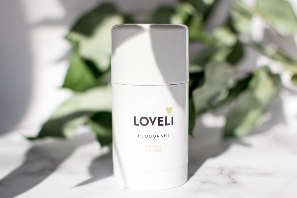 Een witte fles deodorant is omgeven door groene bladeren.