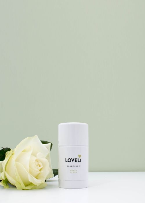 Een witte deodorantstick ligt naast een witte roos op een tafel.