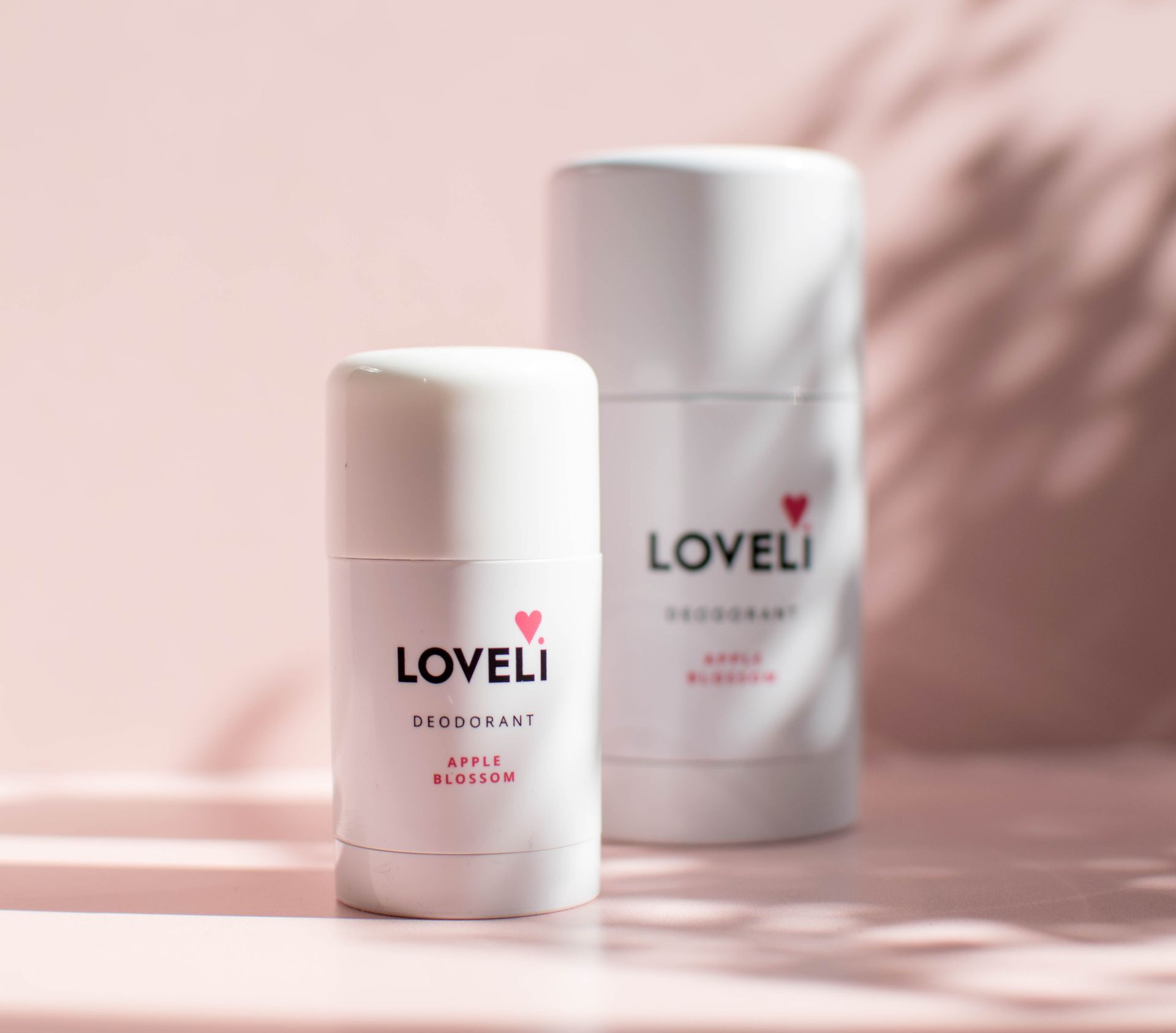 Twee flessen Loveli-deodorant staan op een roze tafel.