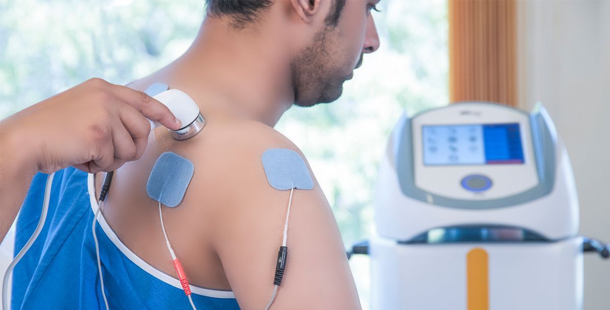 A man is getting a massage with electrodes on his shoulder.