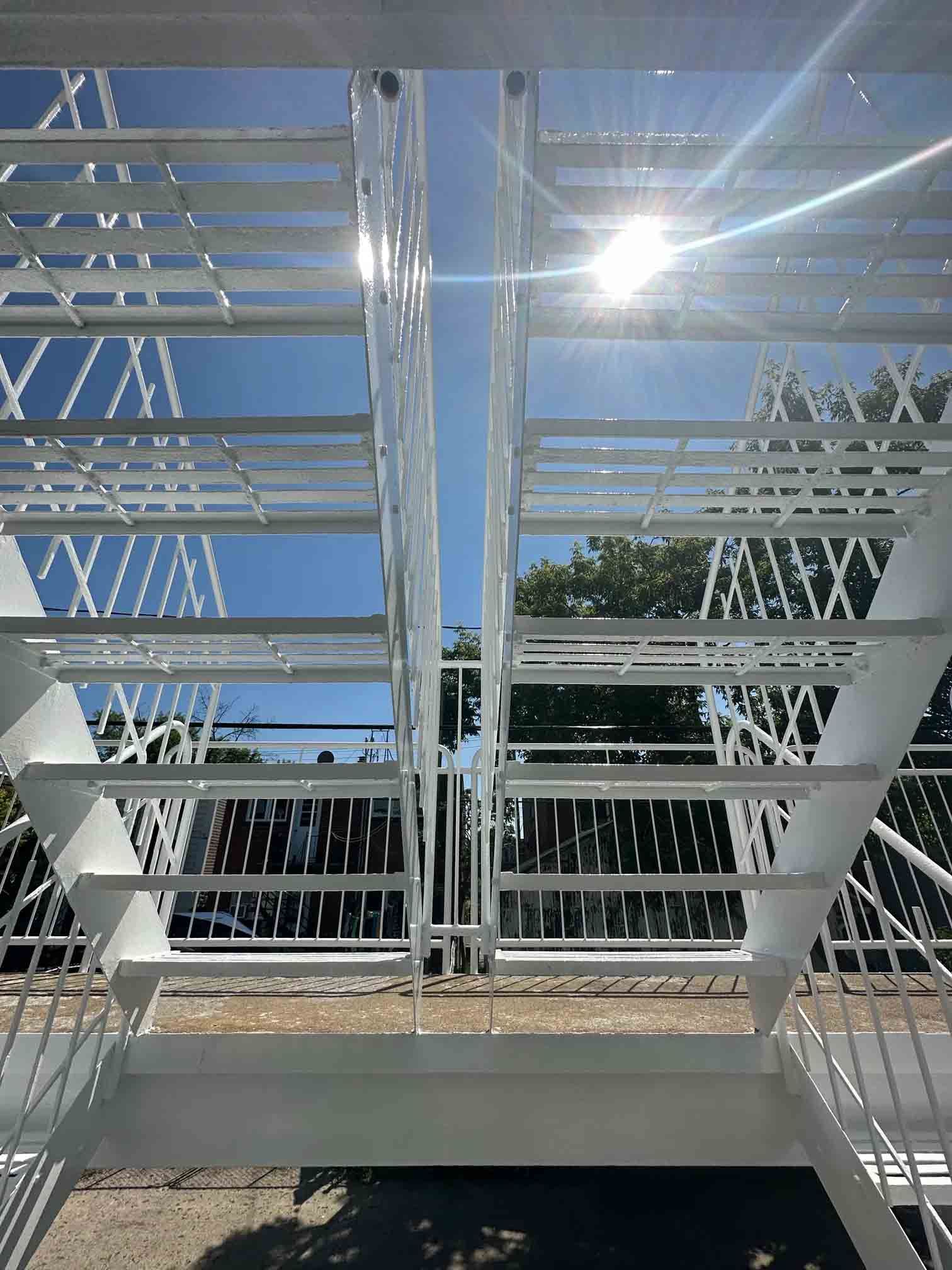 Escalier métallique avec rampes blanches et reflets du soleil sur un ciel bleu extérieur