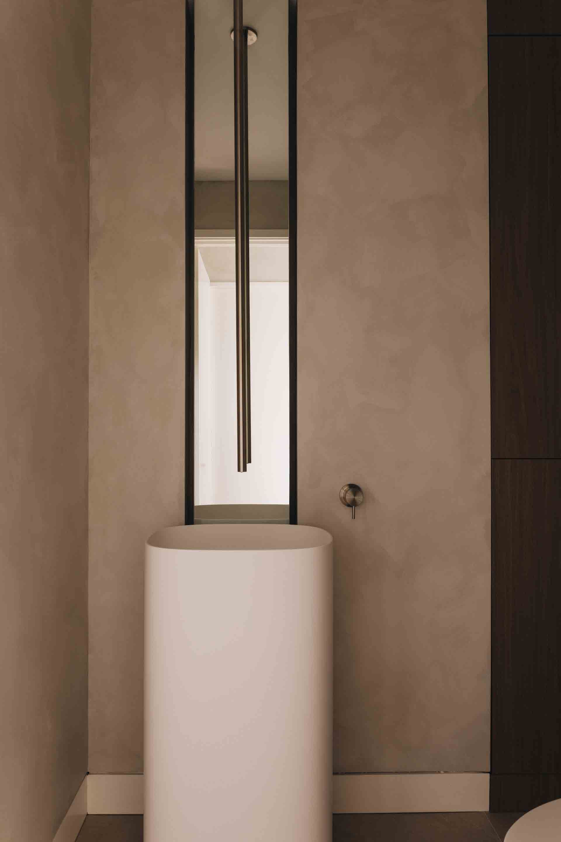 Salle de bains minimaliste avec un grand miroir, un lavabo sur pied blanc et des murs beiges.