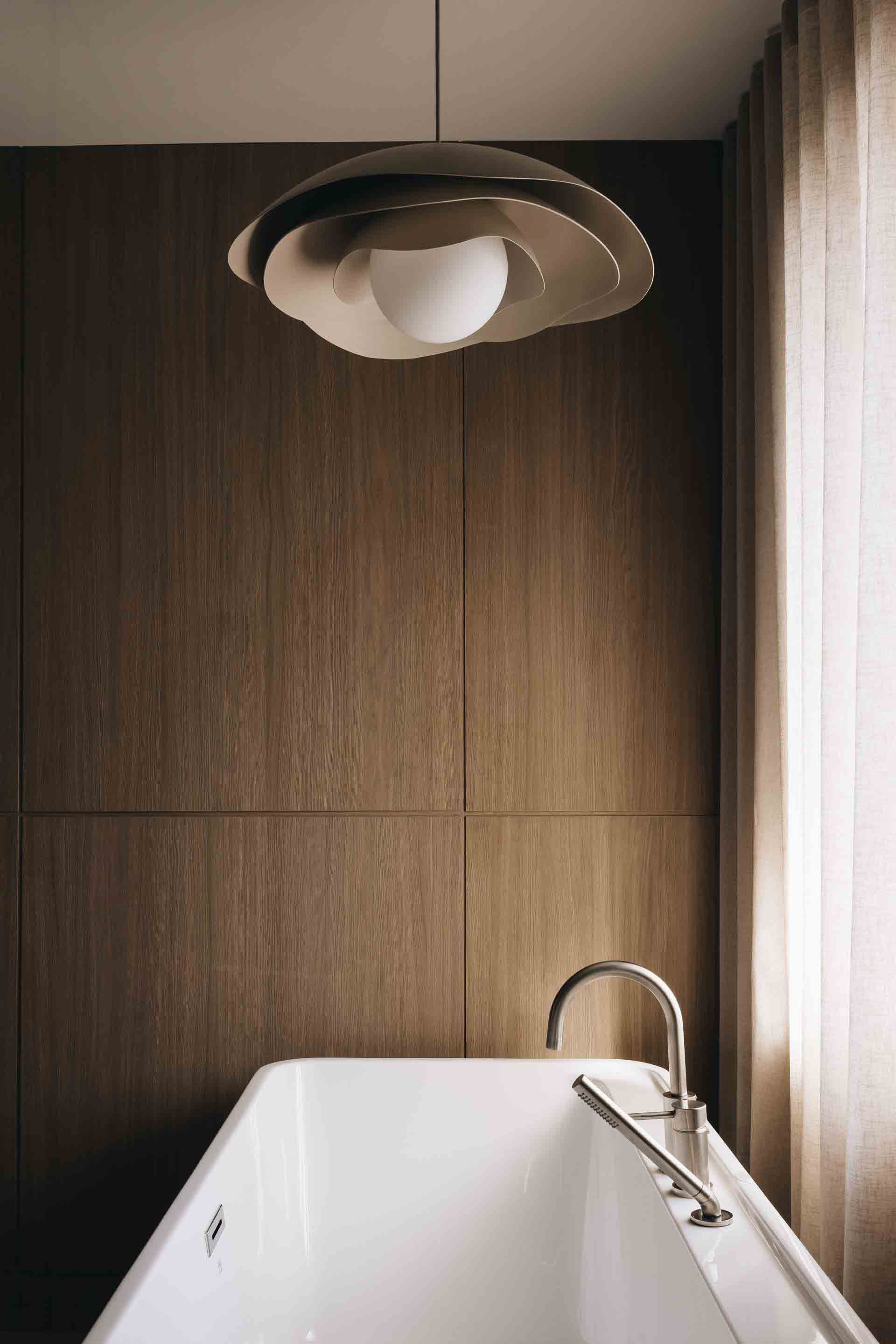 Salle de bains moderne avec baignoire blanche, mur lambrissé et suspension lumineuse.