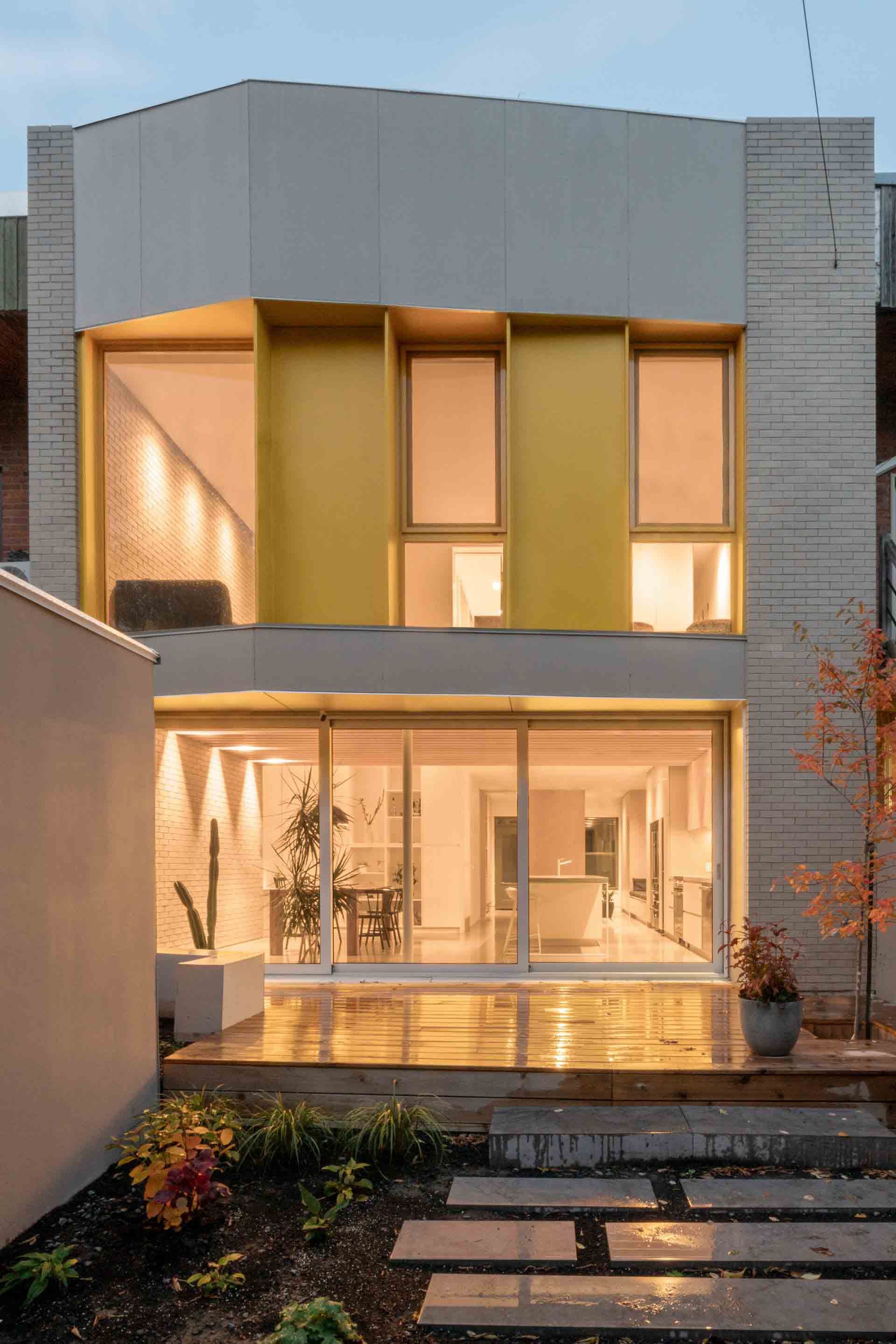 Maison moderne à deux étages avec un éclairage intérieur chaleureux, de grandes fenêtres et une allée en pierre devant