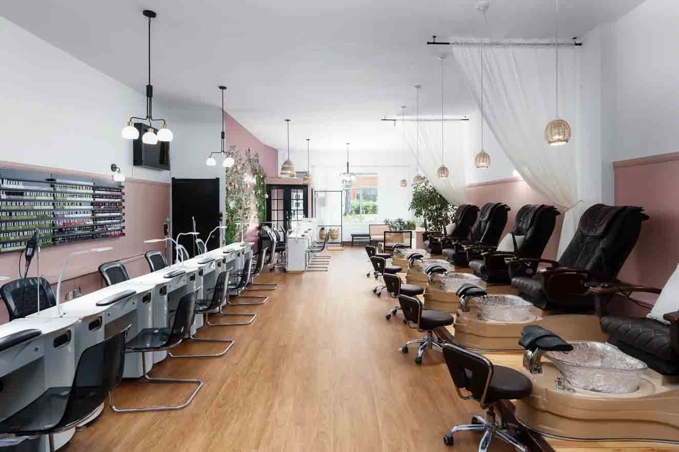 Salon de manucure moderne avec postes de manucure, fauteuils de pédicure et un intérieur lumineux avec parquet en bois.
