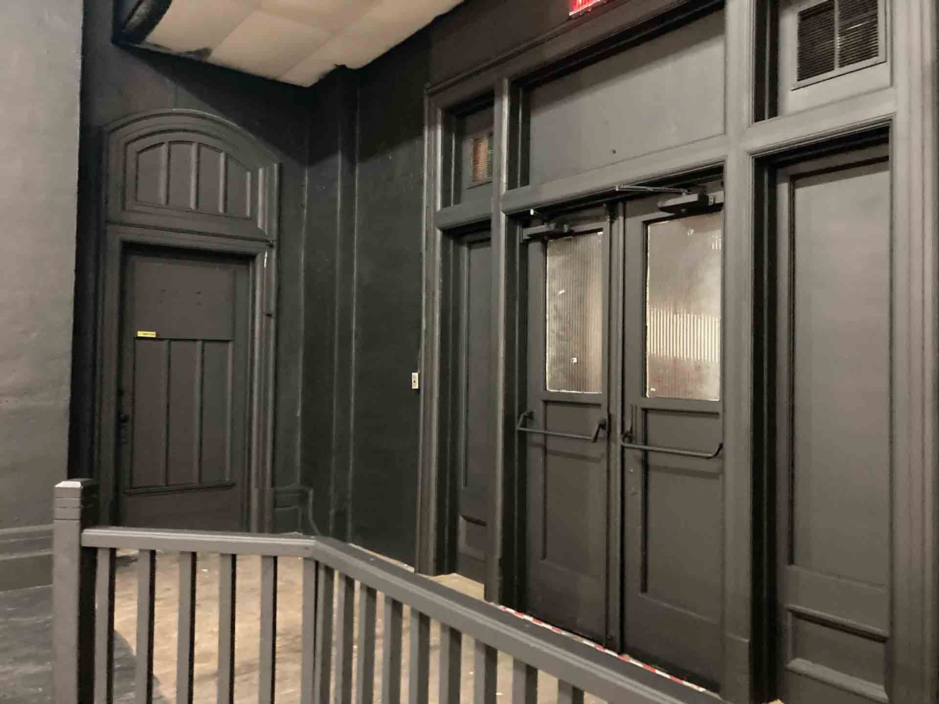 Couloir intérieur gris foncé avec portes à panneaux et rampe métallique sous un plafond éclairé