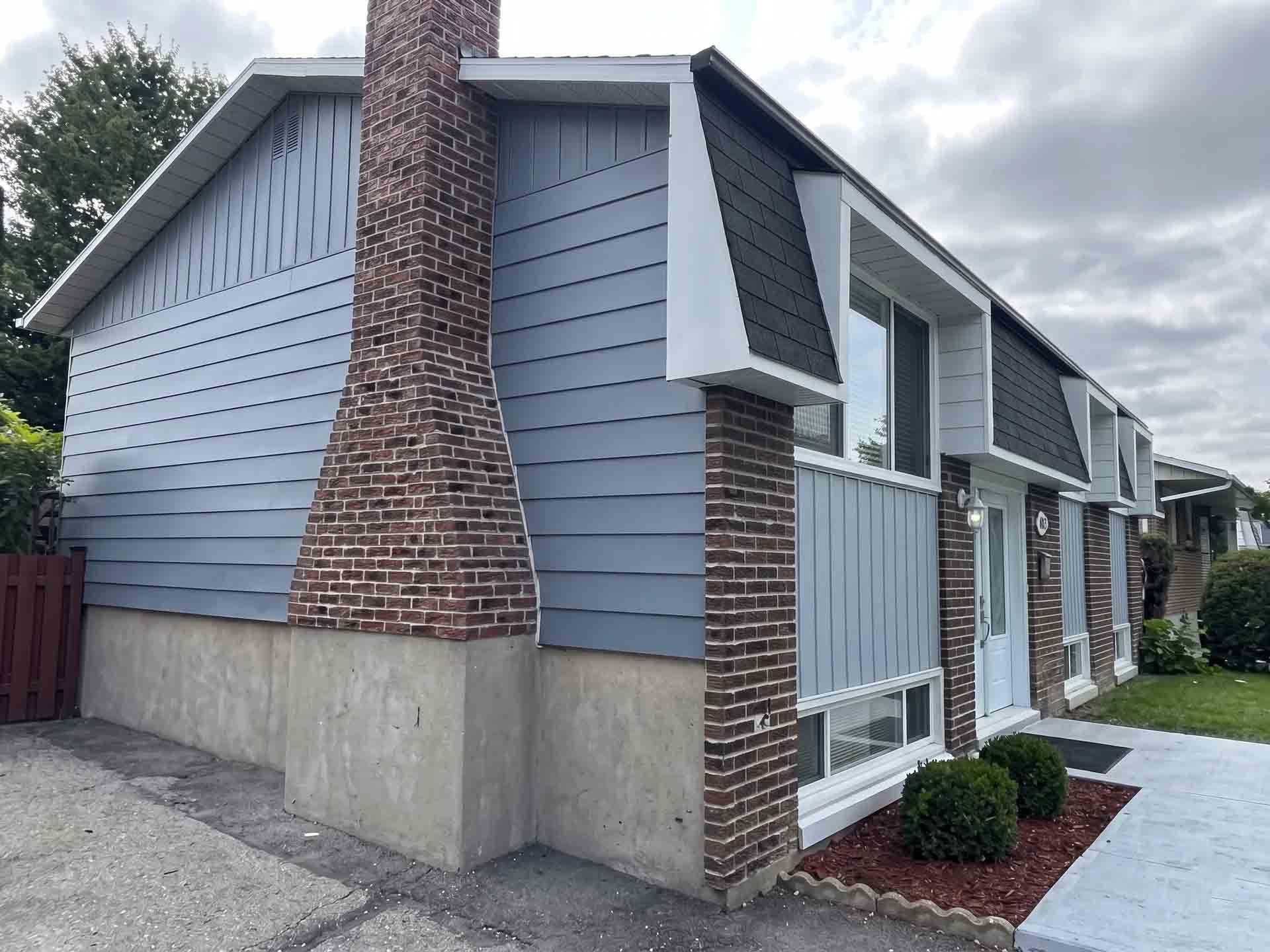 Façade d'un immeuble d'appartements avec bardage bleu, cheminée en briques et balustrades blanches le long d'un trottoir