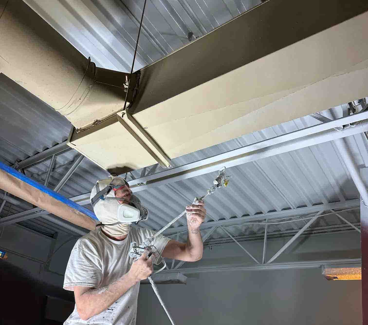 Peintre qui peinture un plafond métallique en blanc